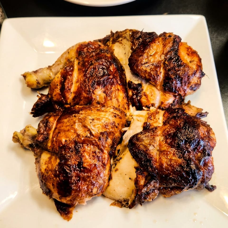 Plate of grilled chicken pieces with charred, golden-brown skin on a restaurant table.