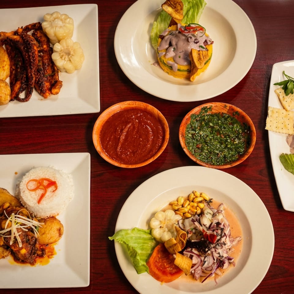 Overhead spread of assorted Peruvian dishes, including grilled octopus, ceviche, rice, potatoes, crackers, and colorful sauces on a wooden table.